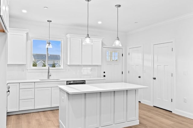 kitchen with white cabinetry, light countertops, ornamental molding, and a sink