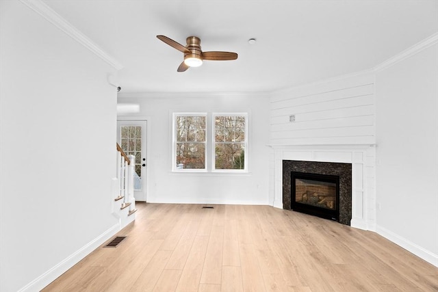 unfurnished living room with visible vents, light wood-style flooring, stairs, a glass covered fireplace, and crown molding