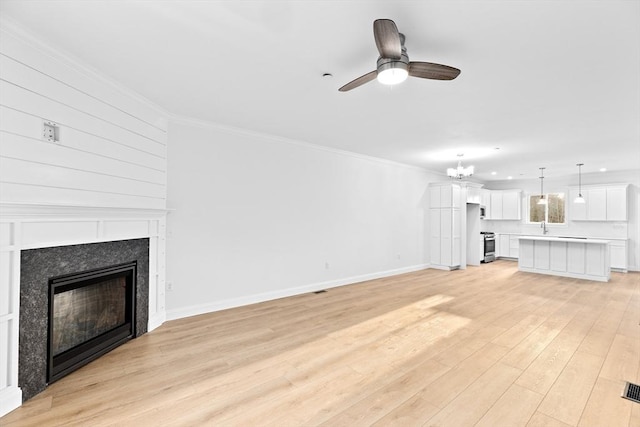 unfurnished living room featuring baseboards, a fireplace, ornamental molding, light wood-style floors, and ceiling fan with notable chandelier