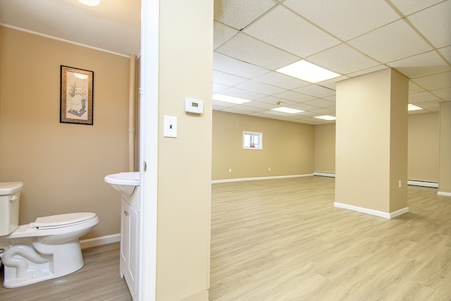 basement with a drop ceiling, light wood-type flooring, and a baseboard radiator