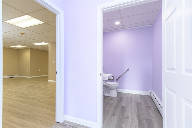 bathroom with a paneled ceiling, hardwood / wood-style flooring, toilet, and a baseboard heating unit