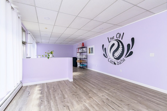 interior space featuring a baseboard radiator, a drop ceiling, and light hardwood / wood-style floors