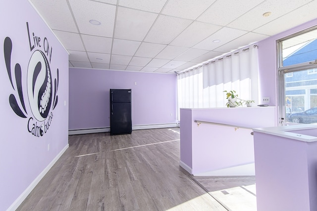 interior space with light hardwood / wood-style flooring, a baseboard radiator, and a drop ceiling