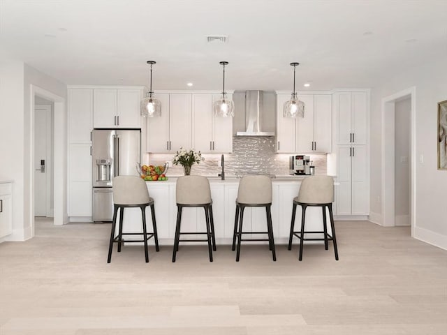 kitchen with white cabinets, high quality fridge, wall chimney exhaust hood, and an island with sink