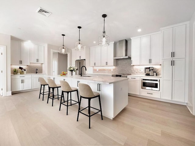 kitchen with white cabinets, a large island, wall chimney range hood, and hanging light fixtures