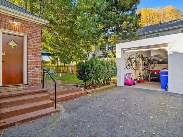 exterior space featuring a garage, driveway, brick siding, and fence