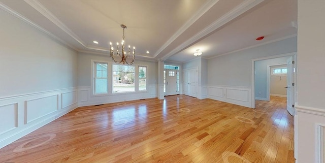 interior space featuring an inviting chandelier, a wealth of natural light, a raised ceiling, and light wood-type flooring