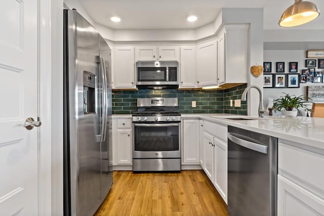 kitchen featuring decorative backsplash, light wood-style floors, white cabinets, stainless steel appliances, and a sink