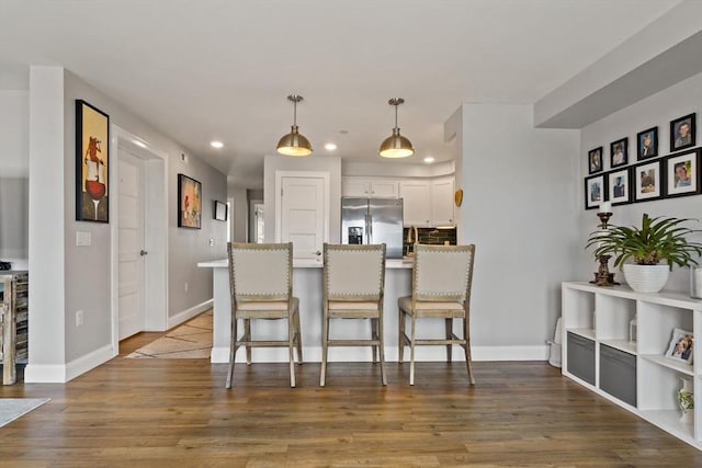 kitchen featuring pendant lighting, stainless steel refrigerator with ice dispenser, wood finished floors, a breakfast bar area, and white cabinets