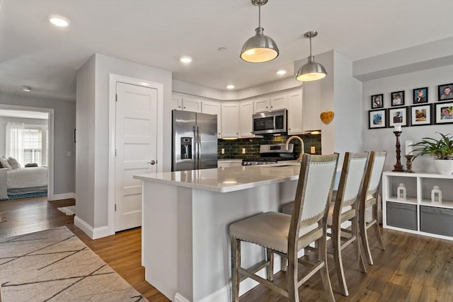 kitchen featuring a breakfast bar, dark wood-style flooring, decorative backsplash, appliances with stainless steel finishes, and white cabinetry