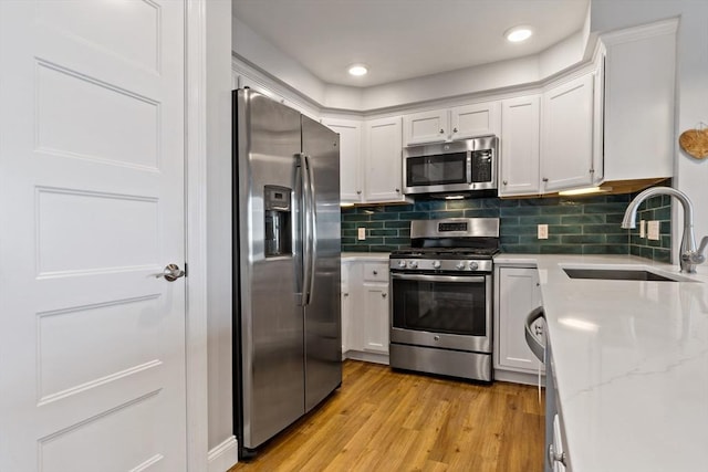 kitchen featuring light wood finished floors, a sink, decorative backsplash, stainless steel appliances, and white cabinetry