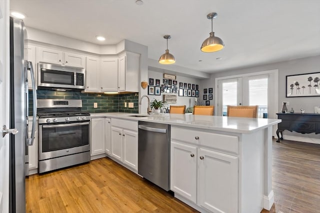 kitchen with white cabinetry, a peninsula, appliances with stainless steel finishes, and a sink