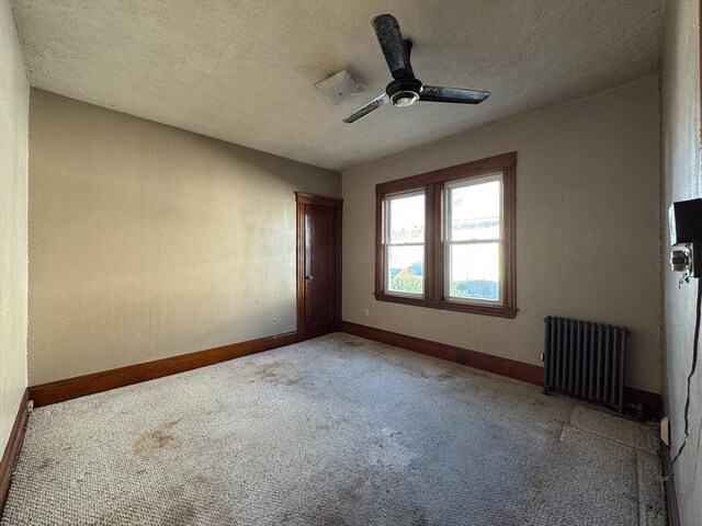 carpeted empty room featuring radiator, ceiling fan, and a textured ceiling