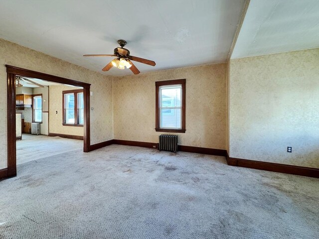 unfurnished room featuring ceiling fan, light colored carpet, and radiator heating unit