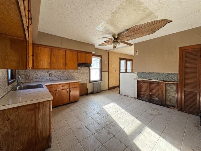 kitchen featuring ceiling fan, sink, light tile patterned flooring, and radiator heating unit