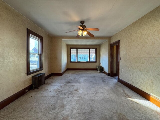 empty room featuring ceiling fan, light colored carpet, and radiator