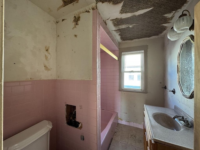 bathroom featuring vanity, a tub to relax in, toilet, and tile walls