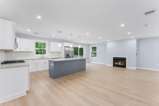 kitchen with light hardwood / wood-style floors, stainless steel refrigerator with ice dispenser, light stone counters, white cabinets, and a kitchen island