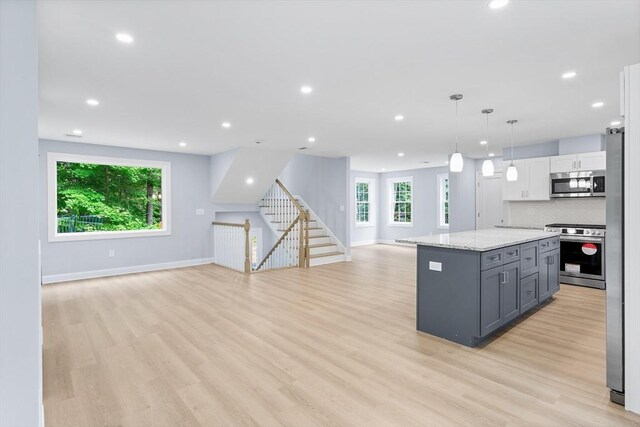 kitchen featuring light wood-type flooring, tasteful backsplash, white cabinets, appliances with stainless steel finishes, and light stone counters