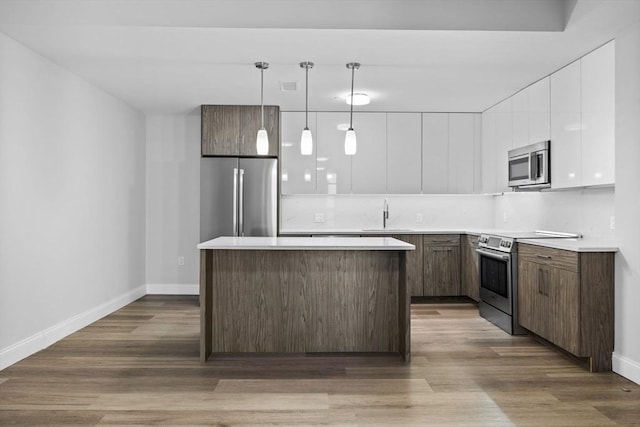 kitchen with white cabinetry, appliances with stainless steel finishes, a kitchen island, and wood finished floors