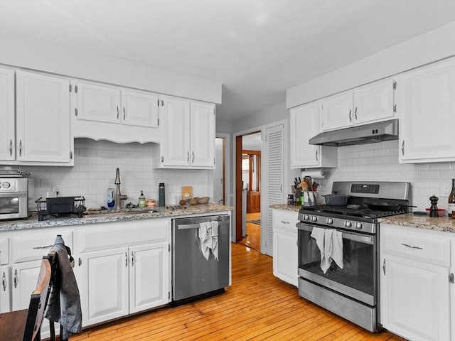 kitchen with a sink, appliances with stainless steel finishes, under cabinet range hood, and white cabinetry