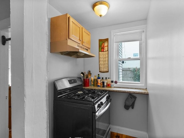 kitchen with light brown cabinetry, baseboards, under cabinet range hood, and gas range