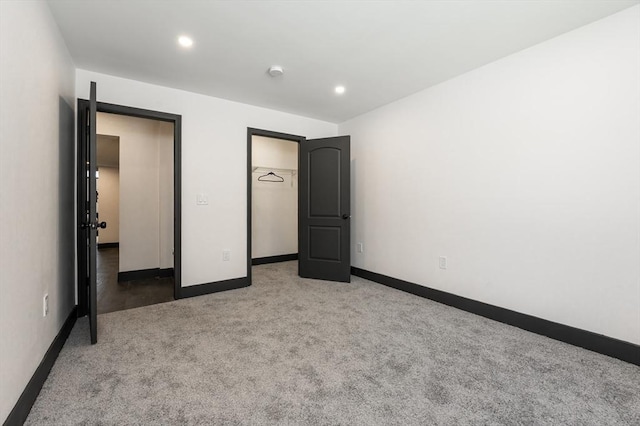 unfurnished bedroom with a walk in closet, a closet, and light carpet