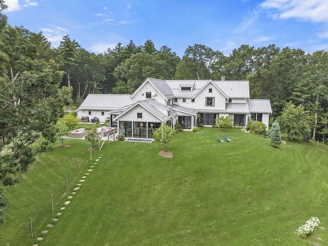 back of property featuring a sunroom, a wooded view, a yard, and a standing seam roof