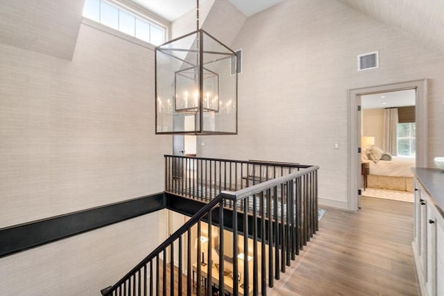 stairway featuring an inviting chandelier, high vaulted ceiling, visible vents, and wood finished floors