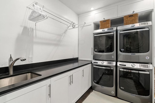 clothes washing area with a sink, cabinet space, wood finished floors, stacked washer and dryer, and washer and dryer