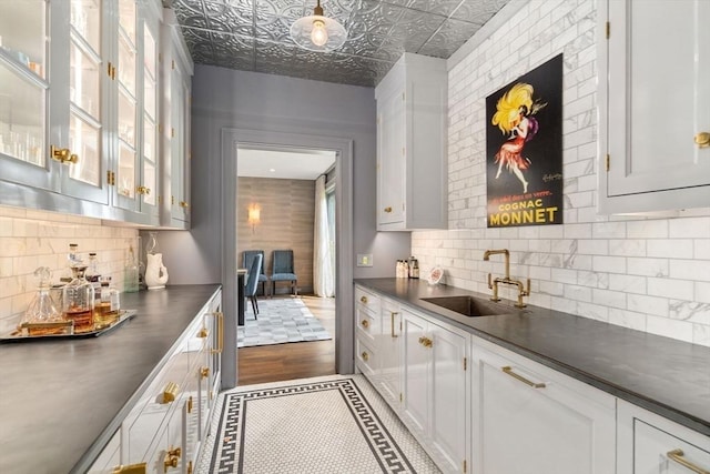 bar with dark wood-style flooring, tasteful backsplash, an ornate ceiling, and a sink