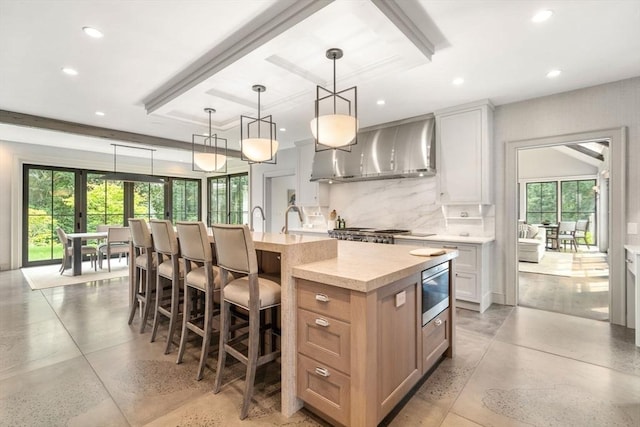 kitchen with wall chimney range hood, decorative backsplash, a large island with sink, and recessed lighting