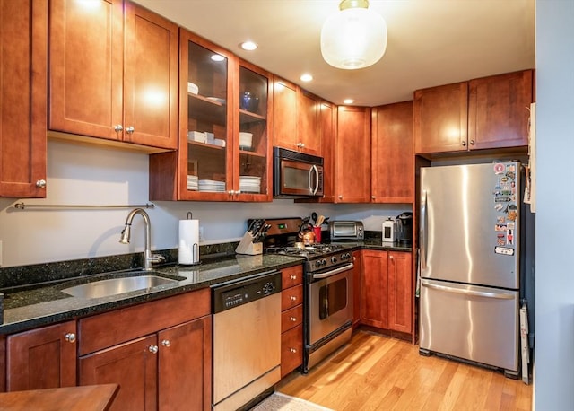 kitchen with stainless steel appliances, a sink, light wood-style floors, glass insert cabinets, and dark stone counters