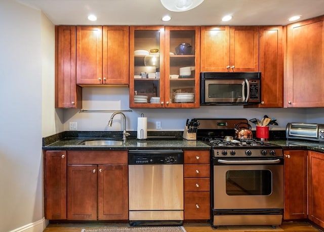 kitchen featuring appliances with stainless steel finishes, a sink, dark stone counters, glass insert cabinets, and recessed lighting