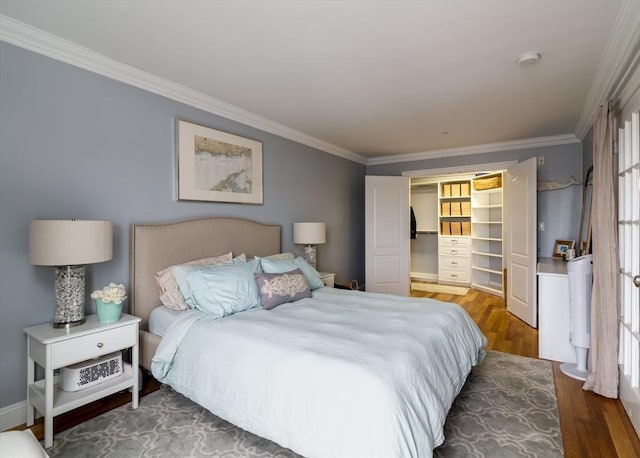 bedroom with ornamental molding, multiple windows, wood finished floors, a walk in closet, and a closet