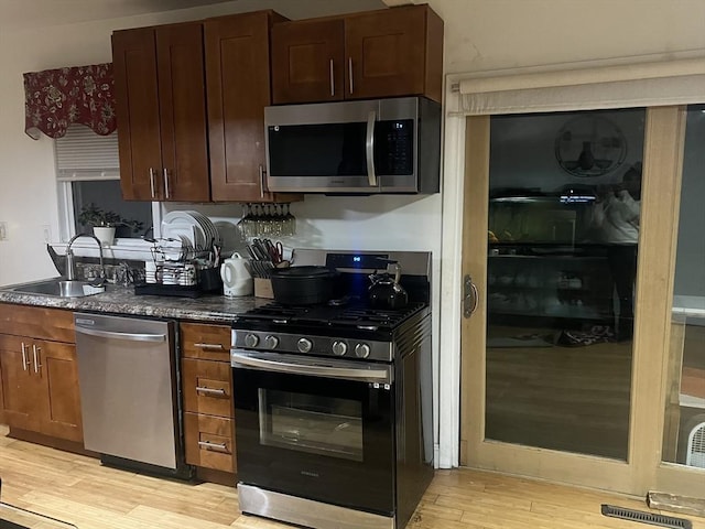 kitchen with appliances with stainless steel finishes, sink, dark stone counters, and light hardwood / wood-style flooring