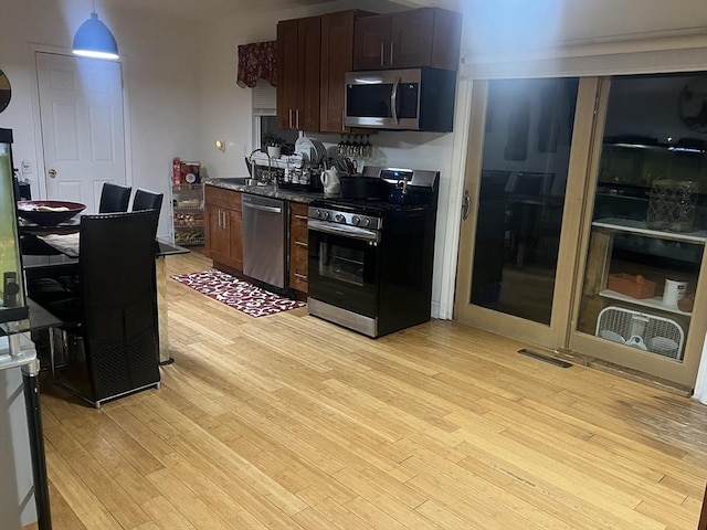 kitchen featuring stainless steel appliances, dark brown cabinets, pendant lighting, and light hardwood / wood-style flooring