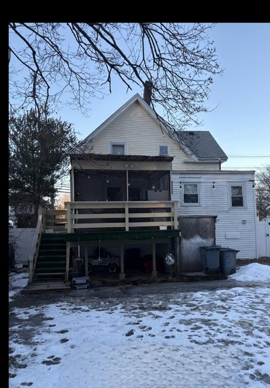 snow covered back of property featuring a wooden deck and a sunroom