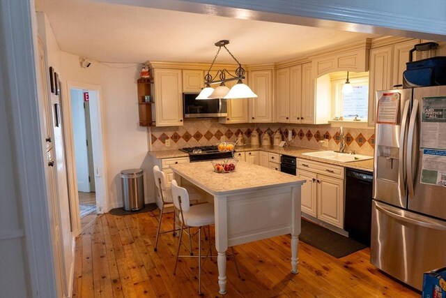 kitchen featuring a breakfast bar, a center island, hanging light fixtures, stainless steel appliances, and a sink