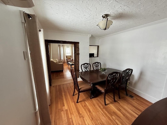 dining area with visible vents, ornamental molding, a textured ceiling, wood finished floors, and baseboards