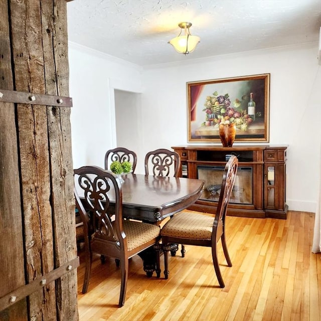 dining space featuring a textured ceiling, a fireplace, baseboards, light wood finished floors, and crown molding