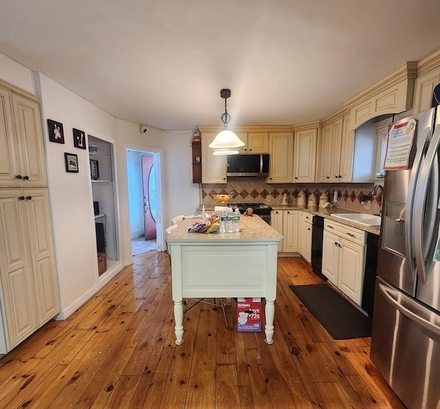 kitchen featuring pendant lighting, cream cabinetry, appliances with stainless steel finishes, a kitchen island, and a sink