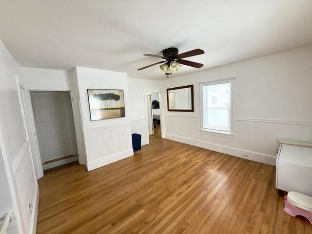 unfurnished bedroom with a wainscoted wall, a ceiling fan, and wood finished floors