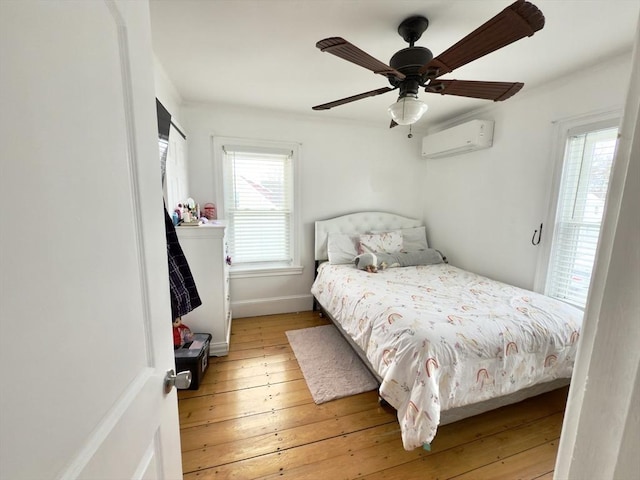 bedroom with light wood finished floors, ceiling fan, baseboards, and a wall mounted AC