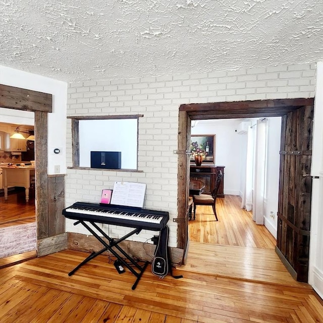 interior space featuring wood-type flooring, a textured ceiling, and brick wall