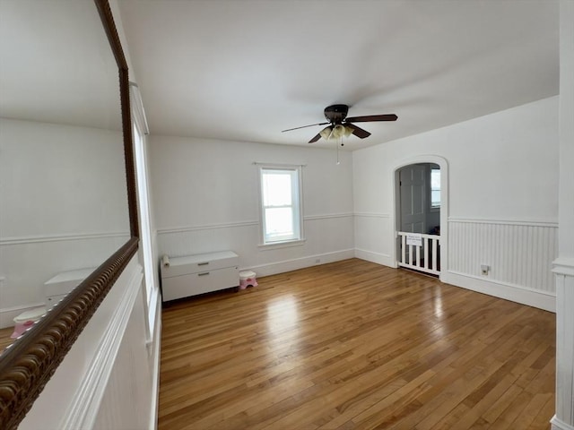 empty room featuring arched walkways, a wainscoted wall, hardwood / wood-style flooring, and a ceiling fan