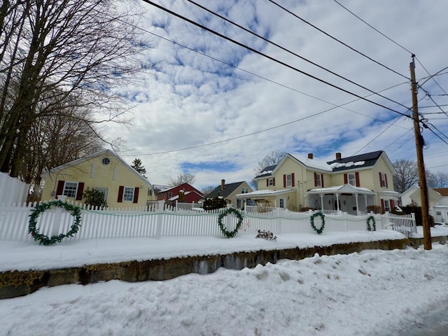 snowy yard with a fenced front yard, a residential view, and covered porch