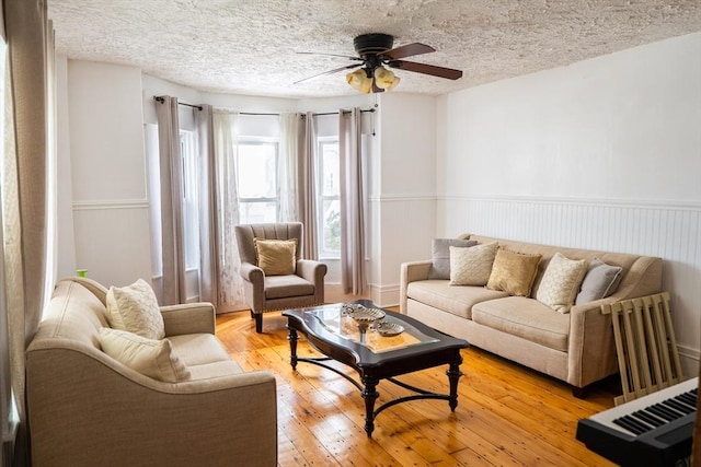 living area featuring a wainscoted wall, ceiling fan, a textured ceiling, and light wood finished floors