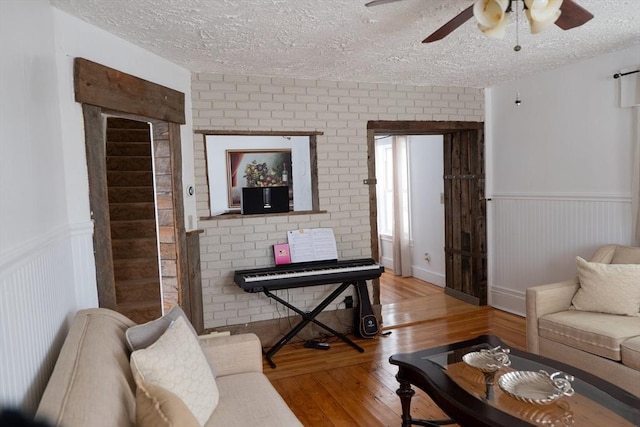 living area featuring light wood-type flooring, wainscoting, ceiling fan, and a textured ceiling