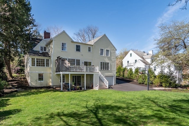 rear view of house with a wooden deck, a lawn, driveway, a chimney, and an attached garage